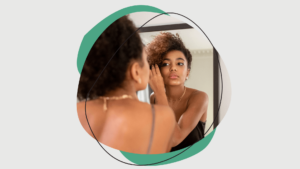 Black woman applying mascara in front of a mirror.